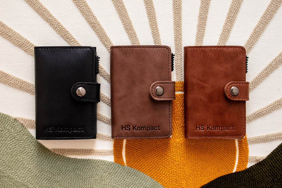 Kompact genuine leather wallets in Black, Dark Brown and Light Brown (left to right) on a cotton surface